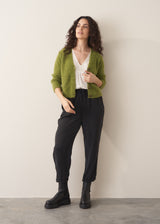 Woman wearing a green marled v-neck cardigan with a white top and black trousers