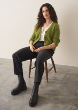 Woman wearing a green marled v-neck cardigan with a white top and black trousers