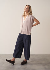 Woman wearing a beige sleeveless button up cardigan with blue jeans