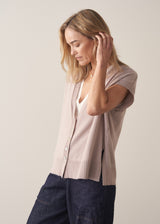 Woman wearing a beige sleeveless button up cardigan with blue jeans