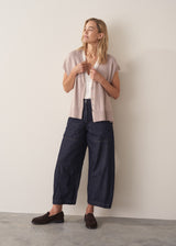 Woman wearing a beige sleeveless button up cardigan with blue jeans