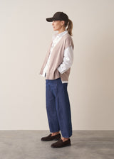 Woman wearing a beige sleeveless button up cardigan with blue jeans