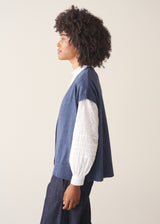 Woman wearing a blue knitted waistcoat, white embroidered top and denim jeans.