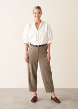 Woman wearing light khaki trousers with a white, puff sleeve shirt and brown leopard loafers.