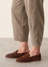 Woman wearing light khaki trousers with a white, puff sleeve shirt and brown leopard loafers.