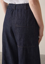 Woman wearing a white shirt and dark blue denim cargo trousers against a plain background