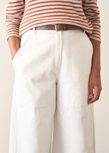 Woman wearing white denim barrel leg trousers with a burnt orange stripe knit sweater and brown belt.