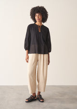 A woman wearing a sheer black embroidered blouse with light linen trousers.