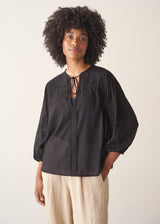 A woman wearing a sheer black embroidered blouse with light linen trousers.