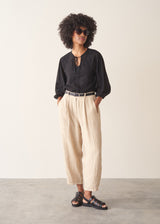 A woman wearing a sheer black embroidered blouse with light linen trousers.