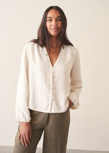 A woman wearing a white long sleeve button-up blouse with a V-neck, paired with khaki green trousers.