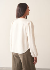 A woman wearing a white long sleeve button-up blouse with a V-neck, paired with khaki green trousers.