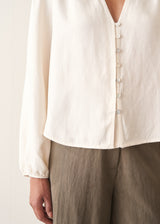 A woman wearing a white long sleeve button-up blouse with a V-neck, paired with khaki green trousers.