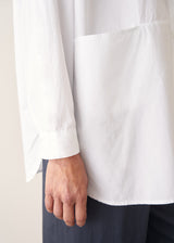 A woman wearing a large white smock shirt with navy blue trousers