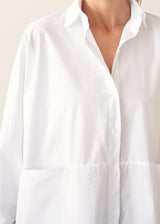 A woman wearing a large white smock shirt with navy blue trousers