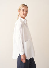 A woman wearing a large white smock shirt with navy blue trousers