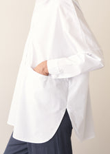 A woman wearing a large white smock shirt with navy blue trousers