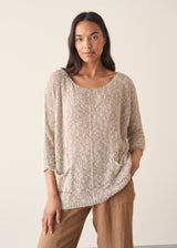 Woman wearing a textured lightweight sweater with linen trousers, against a beige background