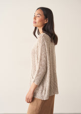 Woman wearing a lightweight beige knitted sweater with camel linen trousers against a beige background