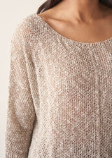 Close up of a woman wearing a lightweight knitted jumper against a beige background