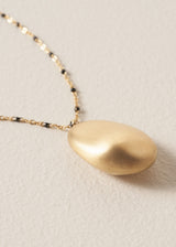 Close up of gold pendant on beaded chain necklace, on a beige background