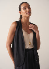 A woman in a silk top and knitted waistcoat wearing a beaded gold chain necklace with a pendant