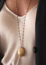 Close-up of women waering a beaded gold chain necklace with pendant, and silk top