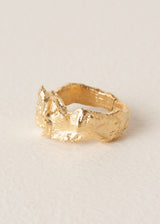 Large, textured molten gold ring on a beige background