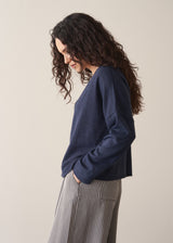 Woman wearing a navy lightweight cardigan with grey striped trousers, against a beige background