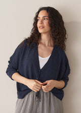 Woman wearing a navy lightweight cardigan with a white tank top and grey striped trousers against a beige background