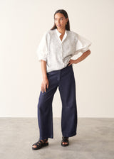 A woman wearing a white-button down cotton shirt with three-quarter puff sleeves and a relaxed fit, with blue denim jeans.