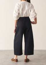 Woman wearing a white shirt and cropped, black barrel-leg denim jeans with leopard print loafers, facing a beige wall