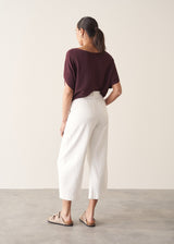 Woman wearing white cropped barrel leg jeans with plum short sleeve top