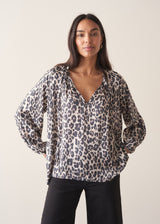 Woman wearing a leopard print blouse and black trousers against a plain background