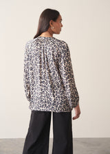 Woman wearing a leopard print blouse and black trousers against a plain background