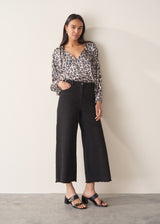 Woman wearing a leopard print blouse and black trousers against a plain background