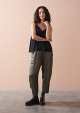 Woman wearing a black satin camisole with lace trim, paired with green satin trousers and Chelsea boots