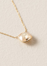 Close up of a round champagne coloured crystal on delicate gold chain necklace, set on a beige background