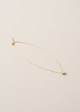 A round champagne coloured crystal on delicate gold chain necklace, placed on a beige background