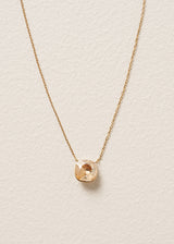A round champagne coloured crystal on delicate gold chain necklace, set on a beige background
