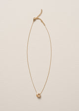 A round champagne coloured crystal on delicate gold chain necklace, laid on a beige background