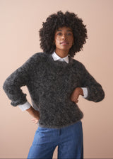 Woman wearing a dark grey fluffy textured sweater with sequin detail, blue jeans and a collared shirt.