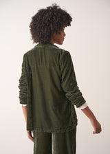 Woman wearing a green velvet blazer and green wide velvet trousers against a white background