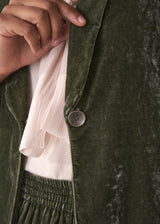 Woman wearing a green velvet blazer and green wide velvet trousers against a white background