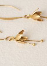 Close up of petal detail on a pair of gold blossom drop earrings, on a beige background