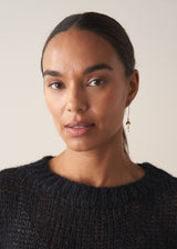 Women wearing gold blossom drop earrings, with black knitted sweater, set against a beige background