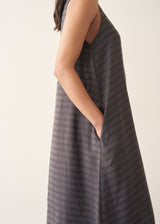 Woman wearing a long, dark gray dress with textured stripes against a plain background
