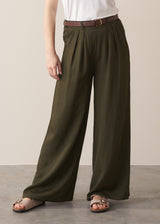 Close up of woman wearing dark green wide leg trousers and neutral sandals against a beige background