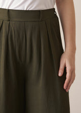 Woman wearing dark green linen blend wide leg trousers and white top against a beige background