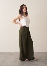 Woman wearing dark green wide leg trousers and white tank with neutral sandals, against a beige background